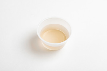 A fresh urine sample in a small round plastic cup container set on a plain white paper background.