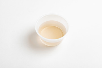 A fresh urine sample in a small round plastic cup container set on a plain white paper background.