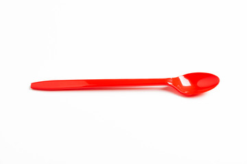 A single long and unused shiny red plastic spoon deliberately and artistically set on a plain white background.