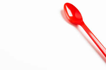 A single long and unused shiny red plastic spoon deliberately and artistically set on a plain white...