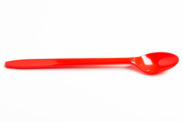 A single long and unused shiny red plastic spoon deliberately and artistically set on a plain white background.