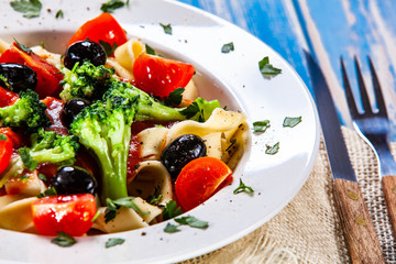 Pasta with herbs and vegetables on wooden background