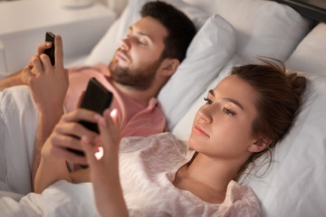 Obraz na płótnie Canvas technology, internet and communication concept - couple using smartphones in bed at night