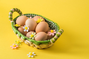 Close up. Easter still life. Rustic eggs in a wicker basket lined with checkered fabric. Yellow background. Copy space.
