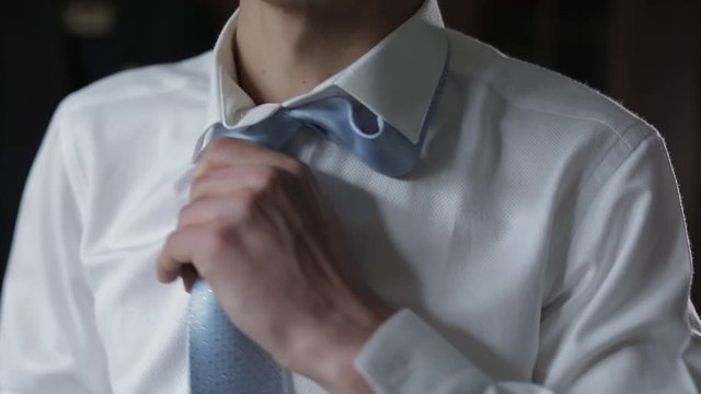 Handsome groom fixes his blue bow tie. Wedding morning. Businessman