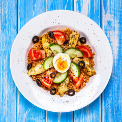Grilled chicken meat with groats and boiled egg on wooden table