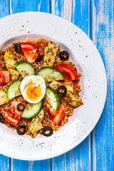 Grilled chicken meat with groats and boiled egg on wooden table