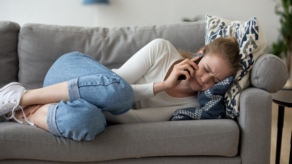 Frustrated woman lying on couch, talk on phone, hearing bad news