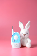Modern baby monitor with toy on color background