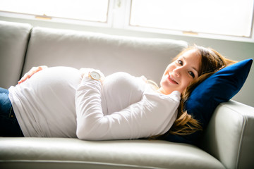 A happy pregnant woman lying on sofa at home