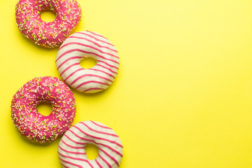 Fototapeta na wymiar Assorted colorful donuts on yellow background, pink glazed and sprinkles donuts. Dessert, sugar food concept