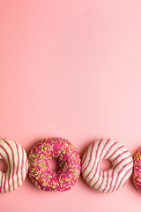 Creative layout made of pink glazed donuts. Flat lay. Food concept. Macro concept. Various decorated doughnuts on soft pink background. Sweet and colourful doughnuts 