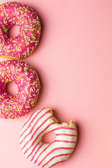 Creative layout made of pink glazed donuts. Flat lay. Food concept. Macro concept. Various decorated doughnuts on soft pink background. Sweet and colourful doughnuts 