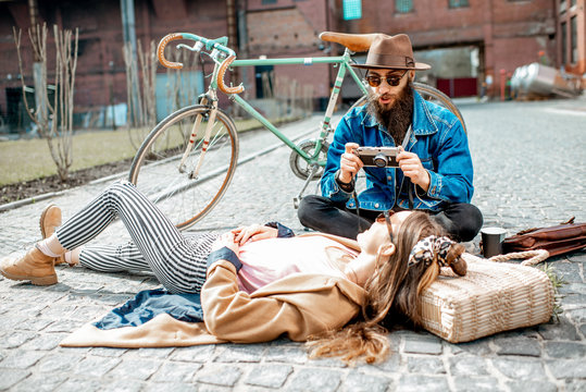 Stylish man photographing young woman lying on the street, having fun together on the urban background