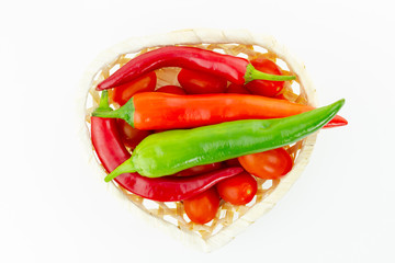 figured wicker basket mix of cherry tomatoes large pods of hot peppers and red chili pods on white background
