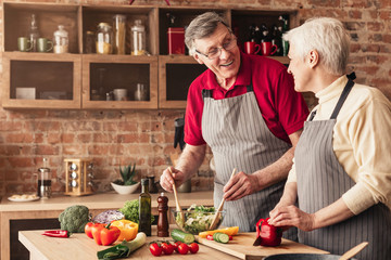 Senior couple preparing fresh salad in kitchen