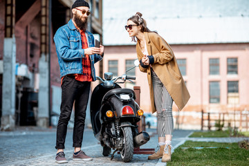 Stylish young man and woman talking together, standing near the retro moped outdoors on the...