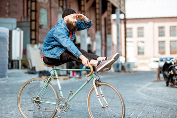 Stylish man as a crazy hipster having fun, riding retro bicycle outdoors on the industrial urban background