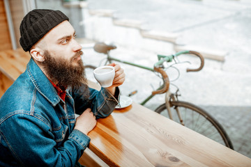 Stylish man enjoying a coffee drink while sitting at the cafe near the window with retro bicycle outdoors