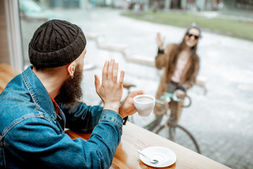 Stylish man meeting his girlfriend with bicycle while sitting with coffee near the window at the cafe