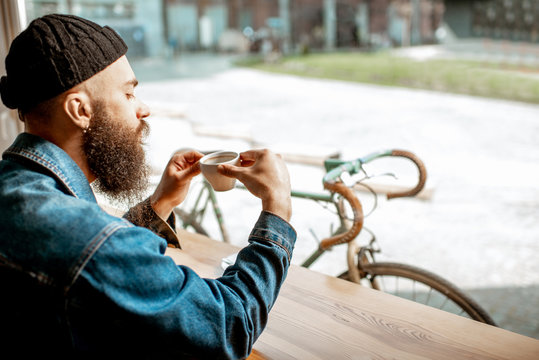 Stylish Man Enjoying A Coffee Drink While Sitting At The Cafe Near The Window With Retro Bicycle Outdoors