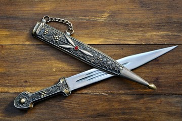 Dagger with ornate pattern on wooden background 
