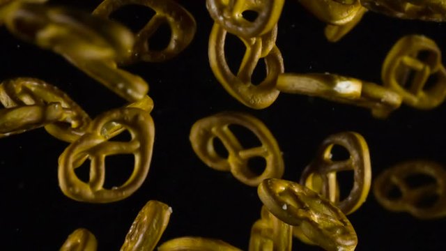 Small Pretzels with Salt. Baked pretzels emerge from the darkness, hovering in front of the camera and then disappear in the shadows. Slow Motion at a rate of 240 fps