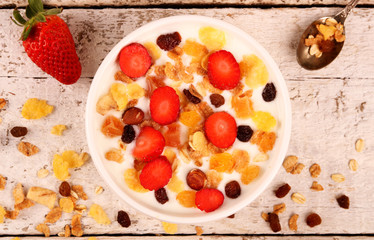 Bowl of yogurt with strawberries and granola muesli, over a white wood background.