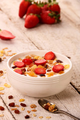 Bowl of yogurt with strawberries and granola muesli, over a white wood background.