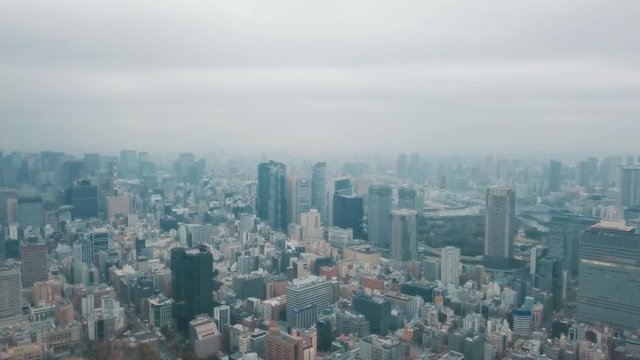 Aerial drone panning up above the Tokyo city skyline in Japan on an overcast day with hazy smog filled skies and grey storm clouds above busy roads and skyscrapers
