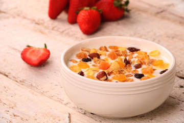 Bowl of yogurt with strawberries and granola muesli, over a white wood background.