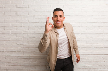 Young latin man cheerful and confident doing ok gesture