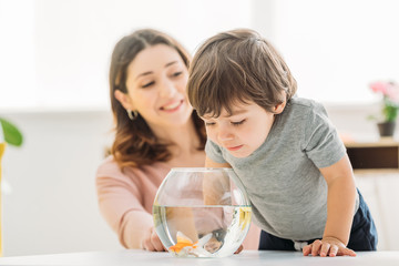 selective focus of adorable child looking into fish bowl near smiling mother