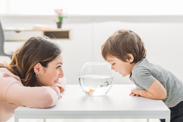 cheerful mother and adorable son looking at fish bowl at home