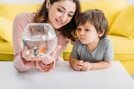 Smiling Mother Holding Fish Bowl Near Adorable Son At Home