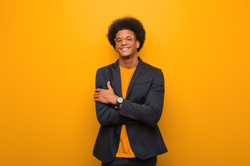 Young business african american man over an orange wall crossing arms, smiling and relaxed
