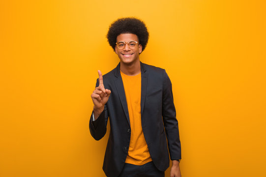 Young business african american man over an orange wall showing number one