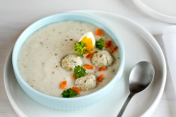 A plate with white Polish soup. White borsch with egg, meatballs, cottage cheese and carrots.