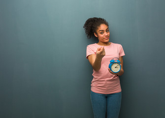 Young black woman inviting to come. She is holding an alarm clock.