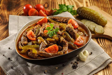 Traditional Tatar dish azu. Fragrant beef meat with tomatoes and pickles in a thick sauce in a plate on a wooden table and natural napkin. Horizontal.
