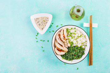 Healthy salad in a white bowl, chopsticks. Chicken rolls, rice, chuka and green onion. Blue background. Asian cuisine. Top view