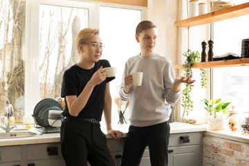 Fototapeta premium Portrait of international gay couple in casual clothes in the morning at home in the kitchen