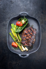 Barbecue dry aged wagyu entrecote beef steak with vegetable and herbs as top view on a gray cast iron pan with copy space