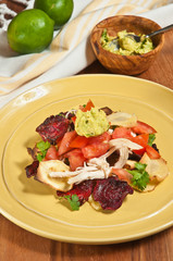 Top view, medium distance of sliced beets, parsnip chip nachos with shredded chicken, sliced tomato,  guacamole, parsley on a round, yellow plate- paleo diet