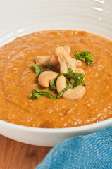 Top view, close up of a bowl of eggplant and tomato soup with  cashew nuts and sliced parsley
