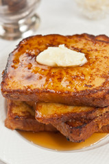 Top view, close distance of three slices fo freshly baked, homemade french toaast with pat of butter and covered with warm, maple syrup on a round white plate