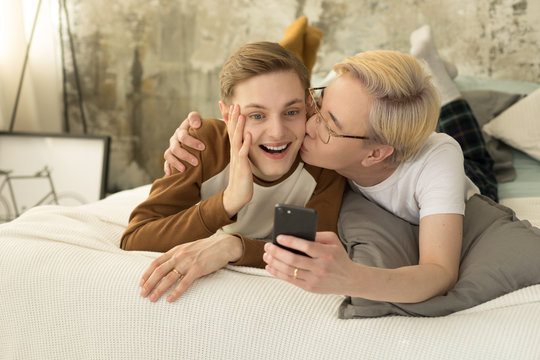 International love. Homosexual asian man with blonde hair kissing his european boyfriend and taking selfie photo