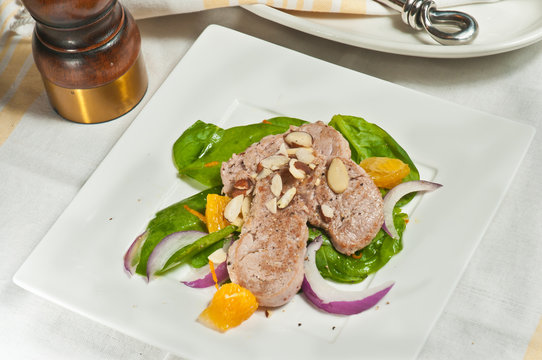 Top View, Medium Distance Of Seared Pork Tenderloin On A Bed Of Freshly Picked Spinach, Sliced Red Onion, Orange Section On A White, Square Plate With Sliced Almonds 