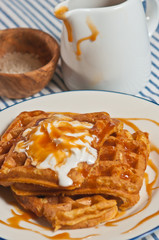 Top view, close distance of a freshly baked, homemade sweet potato waffle  with whipped cream and salted caramel drizzle sauce on a round, white plate with a blue rim 