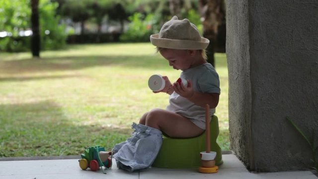 Sweet toddler boy, sitting on potty on a back porch in a holiday resort patio, playing with toys